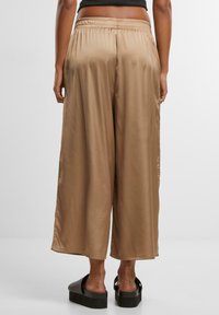Satin, wide-leg pants in a light brown color, featuring an elastic waistband and smooth texture, paired with thick-soled black sandals.