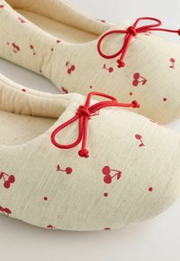 Ballet-loaferit, jotka on valmistettu kevyestä kankaasta, jossa on kerma-valkoinen tausta, punainen kirsikkakuosi ja punaiset sidontakoristeet päällä. Pehmeä, pyöreä muoto.