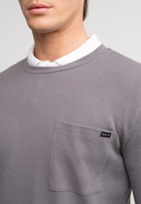 Hallhalli hallide kudumisega pullover, millel on ümmargune kaelus, pikad varrukad ja rinnatasku. Taskul on väike "BIG STAR" silt.