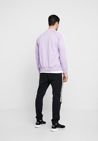 Lavendelfärgad sportjacka med vita ränder, kombinerad med svarta träningsbyxor. Jackan har en ribbad nederkant och ärmar, samt en mjuk textur.