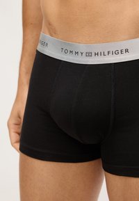 Boxer ajustados de algodón negro con una cinturilla elástica gris que presenta el logo "TOMMY HILFIGER". Costuras bien hechas y diseño ceñido.