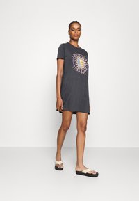 Gray cotton t-shirt dress featuring a colorful sun graphic with swirls and stars. Short sleeves and a relaxed fit. Worn with light sandals.