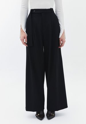 Pantalones de pierna ancha negros, confeccionados en un material suave, con una cintura alta que presenta un botón y un detalle de cinturón atado.