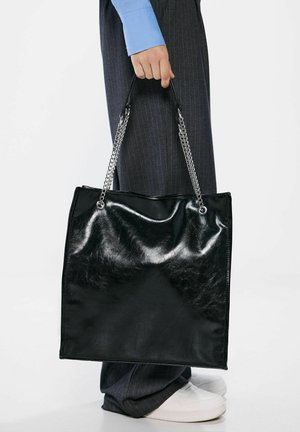 Sac fourre-tout en cuir noir avec une finition brillante, poignées en chaîne argentées, forme rectangulaire, sans motifs ni accents visibles.
