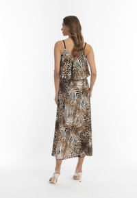 Rochie maxi f�ără mâneci, cu imprimeu animalier în tonuri de maro, având un top cu volane stratificate, cu bretele negre și un design fluid, purtată cu sandale albe cu toc.