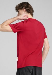 Camiseta de algodón roja con cuello redondo y mangas cortas. Presenta una pequeña etiqueta con el logo de Ferrari en el lado izquierdo, cerca del dobladillo.
