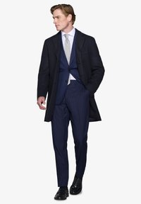Marineblå stribede jakkesæt med et lysegråt slips, lagt under en sort trenchcoat. Polerede sorte sko fuldender det formelle look.