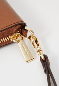 Brun skinnlommebok med gullglidelås og lukkehardware. Inkluderer et metallmerke med inngravert "Michael Kors." Teksturert finish.
