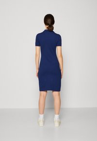 Navyblaues Polokleid aus weichem Stoff, mit taillierter Silhouette und kurzen Ärmeln. Kombiniert mit weißen Socken und Turnschuhen.