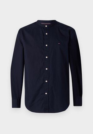 Marineblaue Herrenlangarmshirt mit Stehkragen, weißen Knöpfen vorne und kleinem rot-weiß-blauem Logo auf der Brust.