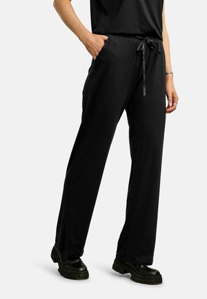 Osoba oblečená v čiernych širokých nohaviciach so zapínaním na šnúrku v páse a bočnými vreckami, v kombinácii s čiernymi robustnými topánkami.