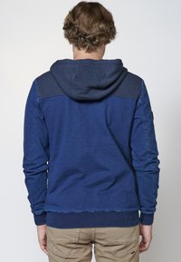 Navy blue hooded sweatshirt with ribbed accents on shoulders, textured hood, and elastic cuffs. Casual fit with frayed hem detail.