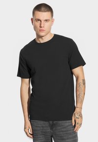 Czarny t-shirt z krótkim rękawem z miękkiej bawełny. Okrągły dekolt i regularny krój. Widoczne tatuaże na przedramionach.