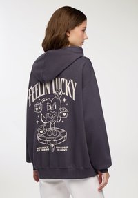 Felpa con cappuccio grigio antracite che presenta una grande grafica sulla schiena di un personaggio da cartone animato con dadi e testo. Vestibilità comoda.