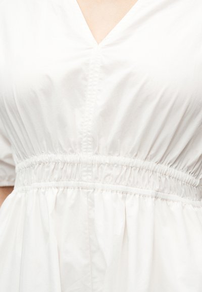 Λευκό φόρεμα με ντεκολτέ σε σχήμα V και κοντά μανίκια, με ελαστική μέση και ροή φούστας. Λείο υλικό με διακριτική λάμψη.