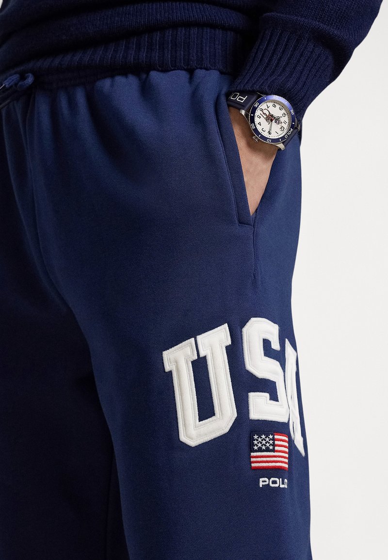 Pantalons de jogging bleu marine avec lettrage blanc "USA" et un patch drapeau américain. Tissu texturé, dotés d'une ceinture à cordon de serrage et de poches latérales.