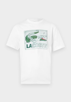 White short-sleeve T-shirt with green and pink embroidered crocodile design and "LACOSTE" text on a grid background on the front.