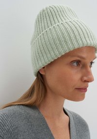Berretto a maglia verde chiaro con righe verticali, caratterizzato da un design aderente. La texture sembra morbida, completata da una forma semplice e pulita.