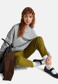 Sweatshirt grigio oversize abbinato a pantaloni verde oliva, calze bianche e ballerine nere. Un maglione marrone è appoggiato su una borsa nera.
