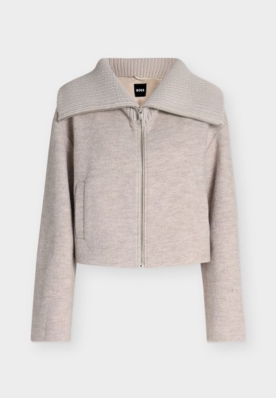 Veste beige clair zippée, manches longues, col large en maille côtelée, poches avant, avec une étiquette noire BOSS à l'intérieur du col.