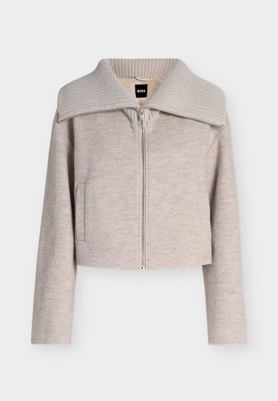 Veste beige clair zippée, manches longues, col large en maille côtelée, poches avant, avec une étiquette noire BOSS à l'intérieur du col.