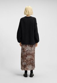 Maglione nero, texturizzato, con maniche oversized, abbinato a una gonna con stampa leopardata e scarpe platform nere chunky. Vista posteriore.