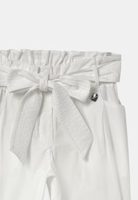 Bílé kalhoty s řaseným elastickým pasem, detailem z vázaného uzlu, dvěma bočními kapsami a malým kovovým akcentem ve tvaru srdce.