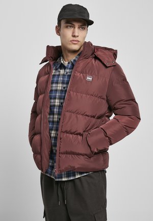 Chaqueta de plumas burdeos con cierre de cremallera frontal, capucha y puños elásticos, llevada sobre una camisa de franela con estampado de cuadros en azul. Material sintético suave, diseño acolchado.