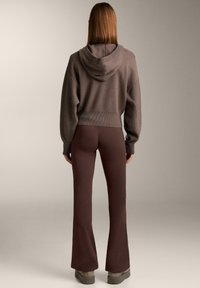 Bruine cropped hoodie met een capuchon, gecombineerd met donkerbruine uitlopende broek. De outfit heeft een zachte textuur en een geribbelde taillebanddetail.