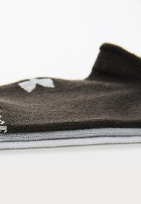 Calcetines marrones y grises apilados, con una base marrón oscuro y un ribete gris claro, además de un logo blanco, mostrando una textura suave.