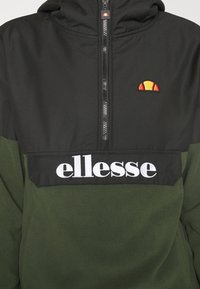 Zielony polarowy pulower z kapturem z czarną górną częścią, zamkiem na pół, haftowanym logo oraz białą naszywką z nazwą na piersi.