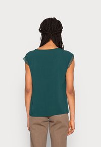 Haut à manches courtes turquoise avec une coupe décontractée et des manches ornées de dentelle, doté d'un col rond et d'une texture de tissu lisse.