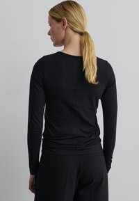 Zwarte langekleurige top met een ronde hals, een aansluitende pasvorm, een gladde textuur en zichtbare stikseldetails, gecombineerd met zwarte broeken.