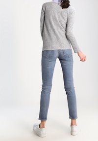Camiseta de manga larga gris claro combinada con jeans ajustados azules claros. El conjunto presenta un diseño sencillo con una estética casual. Zapatillas blancas completan el look.