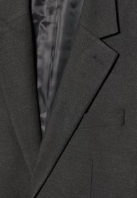 Blazer gris con una textura suave, diseño de un solo botón, solapas con muesca y un brillo sutil. El interior presenta un forro de satén negro.