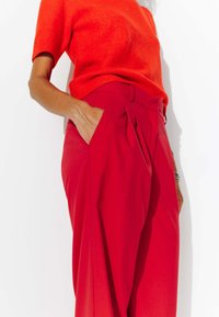 Pull en tricot rouge associé à un pantalon rouge taille haute avec poches latérales et un devant plissé. Le tissu semble doux et texturé.
