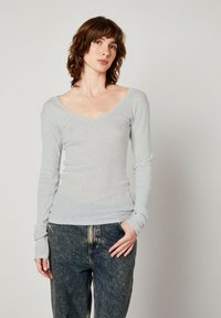 Grå långärmad V-ringad topp i mjukt tyg, figurformad design med en subtil textur och åtsittande ärmslut, kombinerad med blå löst sittande jeans.