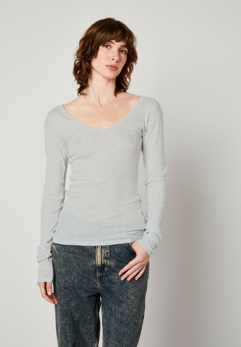 Grå långärmad V-ringad topp i mjukt tyg, figurformad design med en subtil textur och åtsittande ärmslut, kombinerad med blå löst sittande jeans.