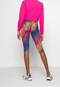 Värgglada ormtryckta leggings i blått, rosa och orange, med en figurnära design. Avslutade med en slät textur och cropped längd.