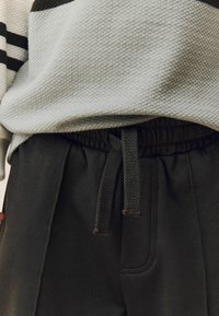 Heller grauer strukturierter Pullover mit schwarzen Streifen, kombiniert mit dunkelgrauen Jogginghosen mit elastischem Bund und Kordelzug.