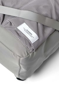 Grå meshväska med en slät, fast botten. Har en texturerad meshtopp och en etikettpatch. Inkluderar ett ljusgrått band för säker stängning.