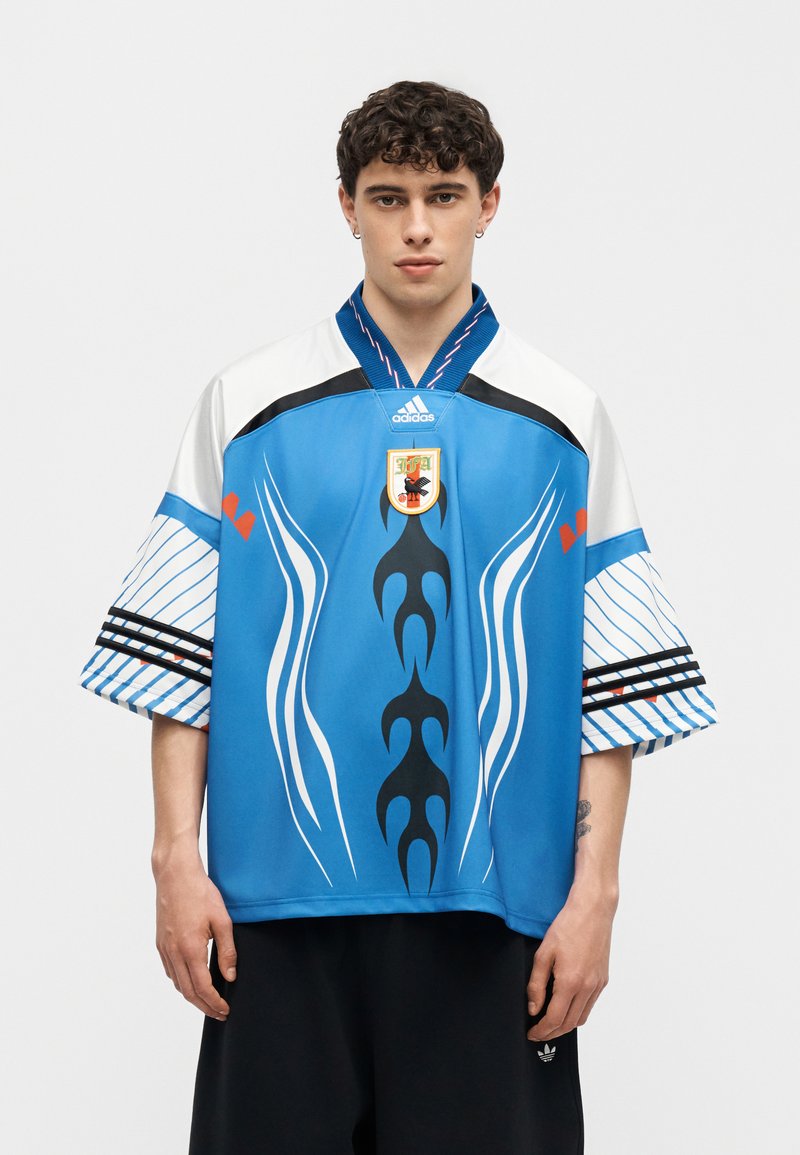 Jeune homme portant un maillot de sport Adidas bleu avec des motifs blancs et noirs et un emblème de la Fédération japonaise de football.
