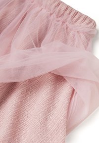 Falda rosa claro con un tejido suave y texturizado, cintura elástica y una superposición de tul transparente en capas, creando un diseño delicado.