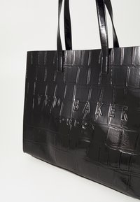 Czarna torebka na ramię z lakierowanej skóry z teksturowanym wzorem krokodyla i wytłoczonym logo "TED BAKER LONDON". Posiada dwie solidne rączki.