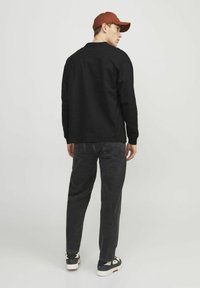 Svart långärmad tröja, grå avslappnade jeans och svarta sneakers med vita detaljer. Personen bär en röd keps, sedd bakifrån.