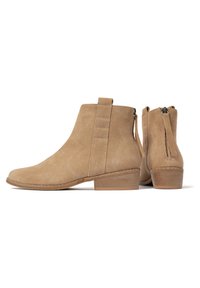 Botines de ante en color arena con puntera ligeramente redondeada, detalles de costura en ángulo, cierre con cremallera y un tacón bajo tipo bloque.
