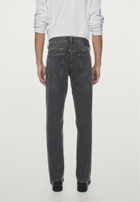 Jeans grigi in denim con taglio a gamba dritta, dotati di tasche applicate, vita con passanti e una texture liscia. Indossati con scarpe nere.