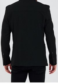 Svart blazer med skräddarsydd passform, strukturerade axlar och fyra knappdetaljer vid ärmarna; tillverkad av ett texturerat tyg.