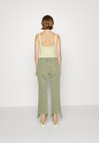 Top sin mangas de color verde claro y vaqueros de pierna ancha verde oliva con dobladillos deshilachados, combinados con zapatillas de plataforma beige. Diseño simple, ajuste casual.
