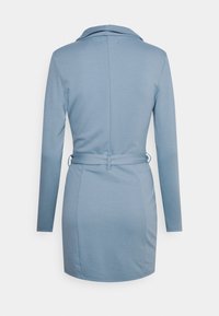 Pitkähihaista mekkoa vaaleansinisestä kankaasta, jossa on kaulus, vyö vyötäröllä ja istuva malli, jonka helma ulottuu hieman polven ylle.